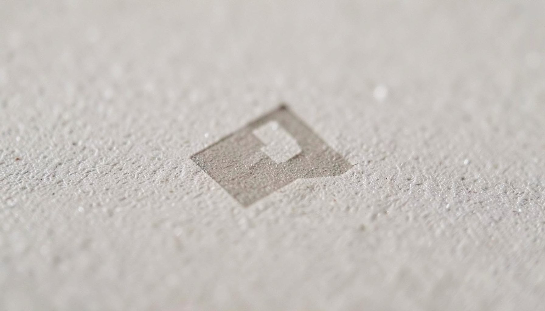 Small minimalist logo mark in muted taupe, simple geometric shape