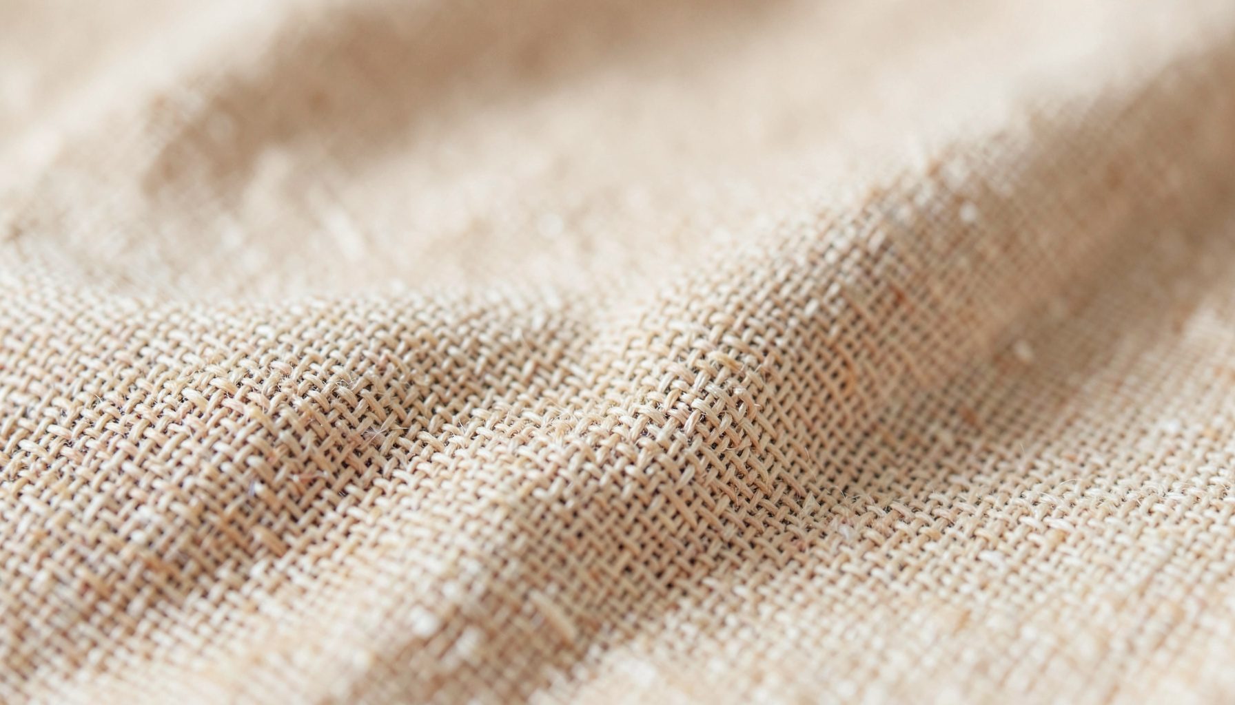 An extreme close-up photograph of woven linen fabric texture in warm beige and cream tones, soft natural light