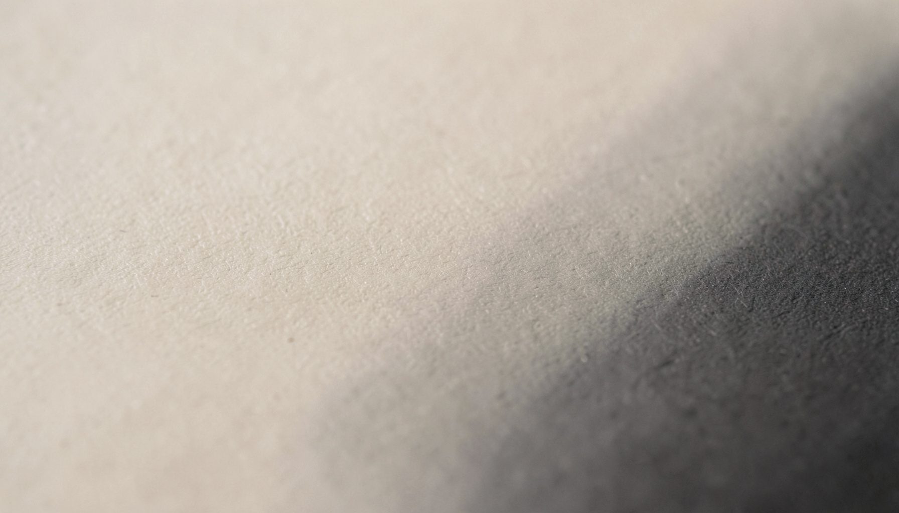 A wide atmospheric photograph of a calm, neutral-toned abstract surface with soft beige and charcoal gradients